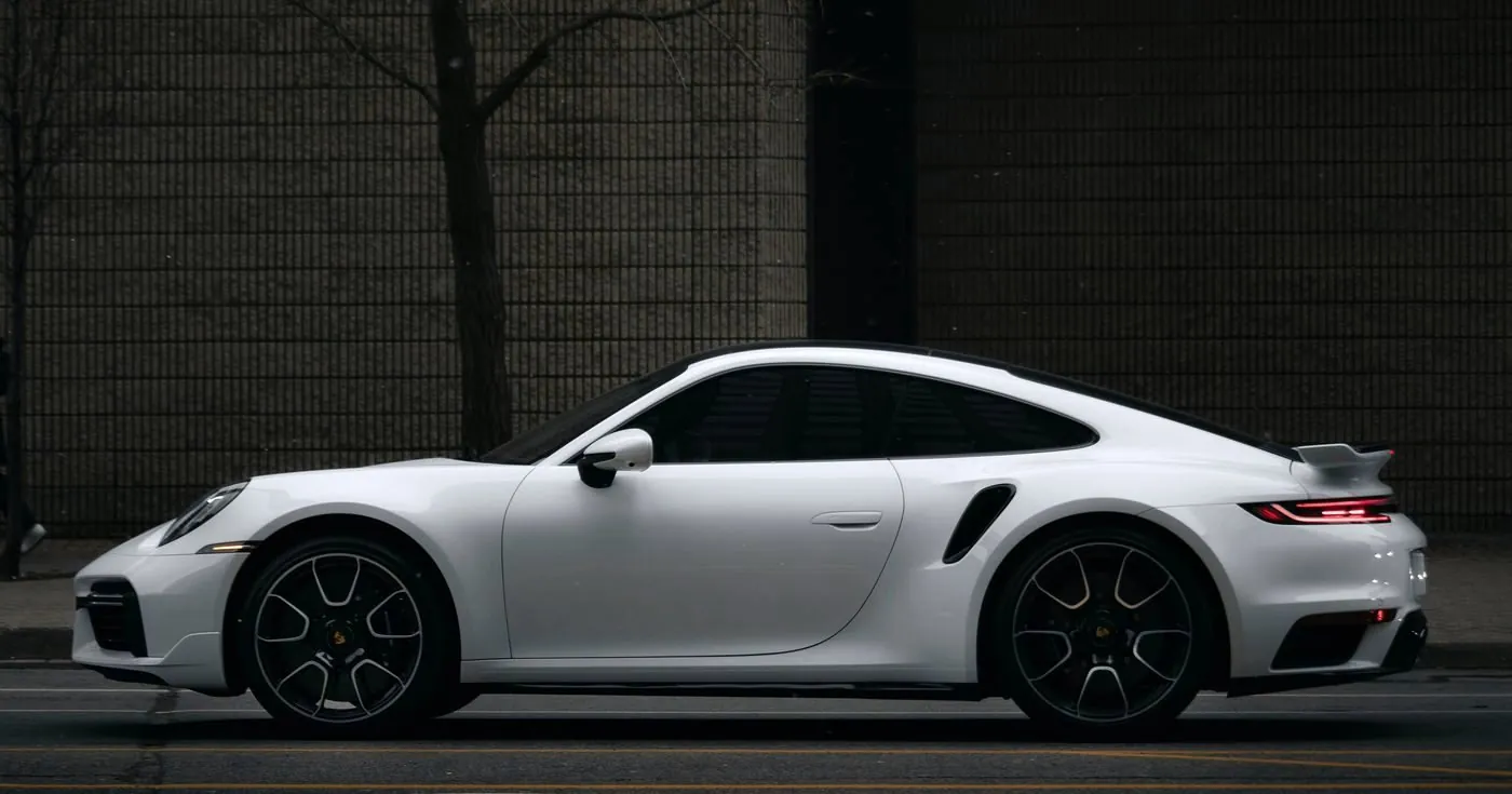 Porsche 911 Turbo S bianca di profilo davanti a un muro di mattoni scuri